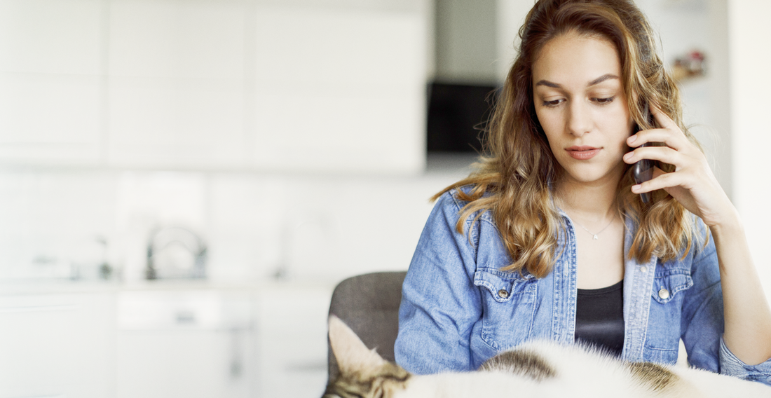 Frau im Jeanshemd sitzt mit einer Katze in einer hellen Küche, teilweise sichtbar.